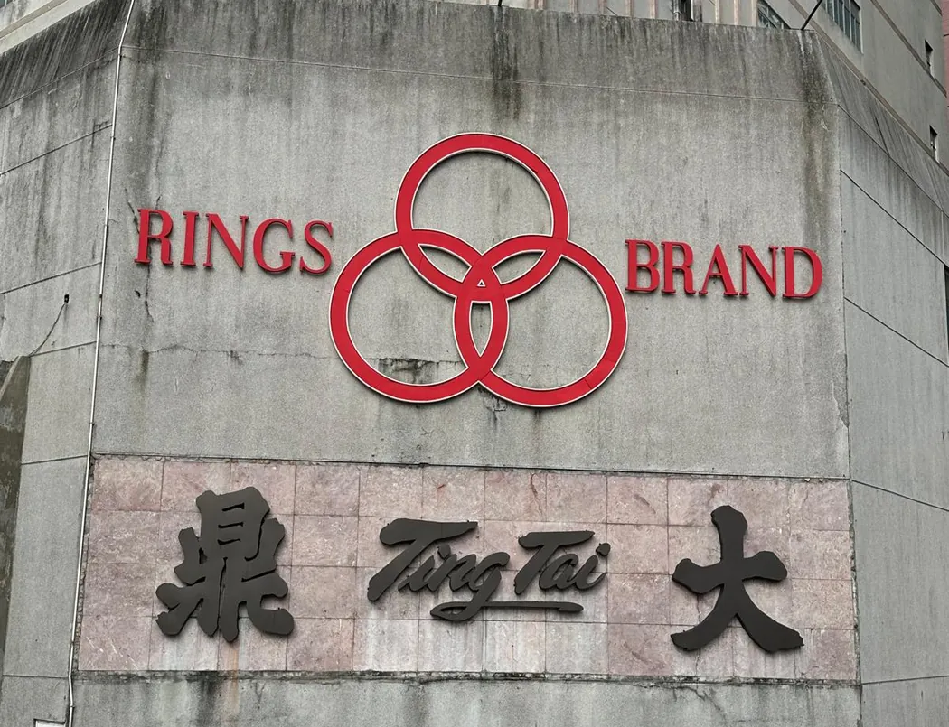 香港一幢大廈外牆上的大型招牌：RINGS 和 BRAND 兩字之間是三個紅圈，下方是「鼎大」二字和 Ting Tai 字樣。