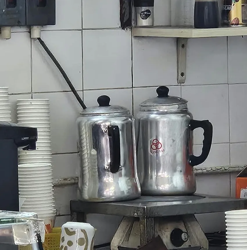 白色瓷磚牆前，爐上放著兩個金屬奶茶壺，右邊的壺身上有三個紅圈。